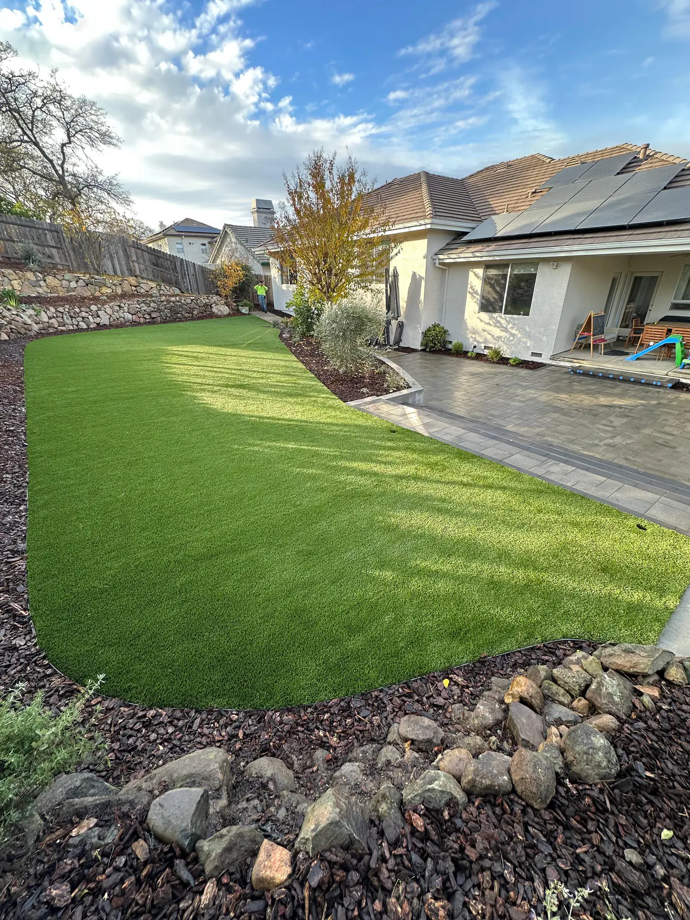 Beautiful residential backyard with stone patio and lush garden, bright natural daylight, airy open green environment