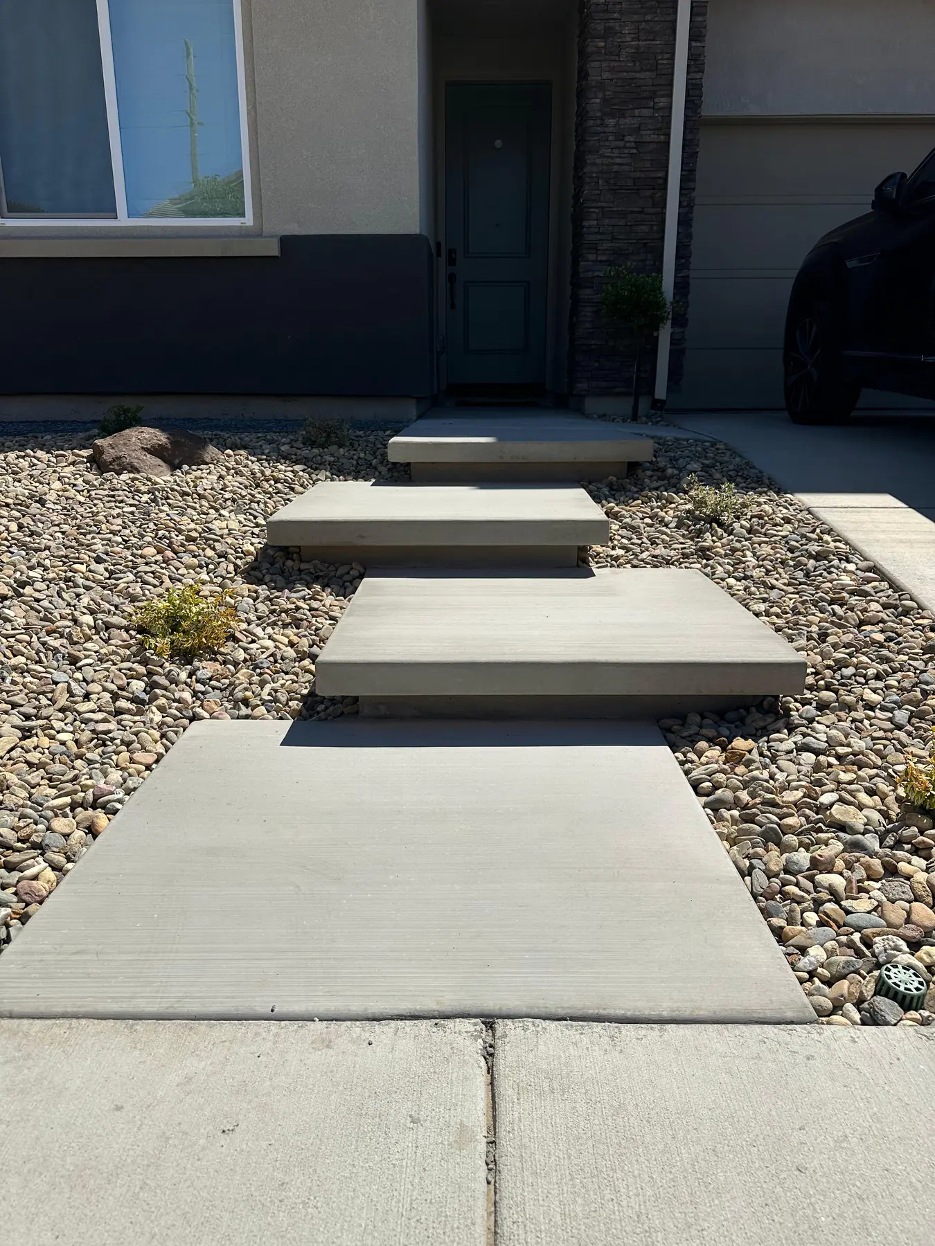 Worker laying grey stone pavers on outdoor pathway in bright daylight, clear open construction environment